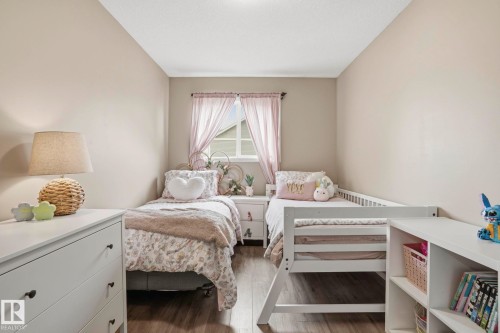 Bedroom featuring two twin beds, wood-finish flooring, a white window frame, and a built-in white shelving unit - 164 150 Edwards Drive, Edmonton, AB - Indoor Photo Showing Bedroom