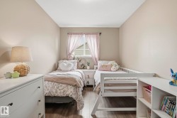 Bedroom featuring two twin beds, wood-finish flooring, a white window frame, and a built-in white shelving unit - 