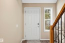 Entryway featuring a six-panel door with smart lock, vertical window, wood-finish flooring, and a staircase with wood handrail and black metal balusters - 164 150 Edwards Drive, Edmonton, AB  - Indoor Photo Showing Other Room 