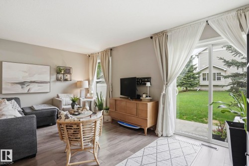 Spacious living area featuring wood-finish flooring, light neutral wall tones, and a sliding glass door providing outdoor access - 164 150 Edwards Drive, Edmonton, AB - Indoor Photo Showing Living Room