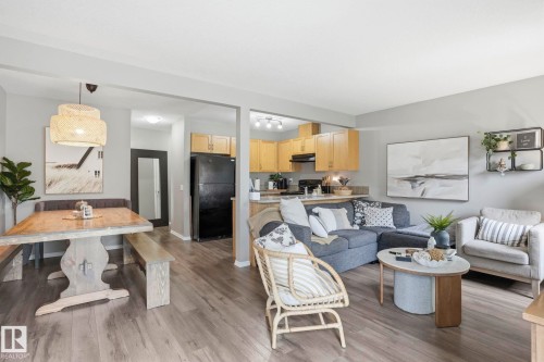 Open-concept living space featuring wood-finish flooring, a kitchen with light wood cabinetry, and a dining area with a statement pendant light - 164 150 Edwards Drive, Edmonton, AB - Indoor Photo Showing Living Room