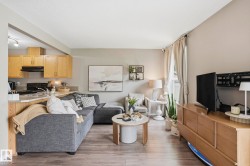 Open-concept living area featuring wood-finish flooring, a kitchen pass-through with a built-in countertop, light wood cabinetry, and a window with drapery - 