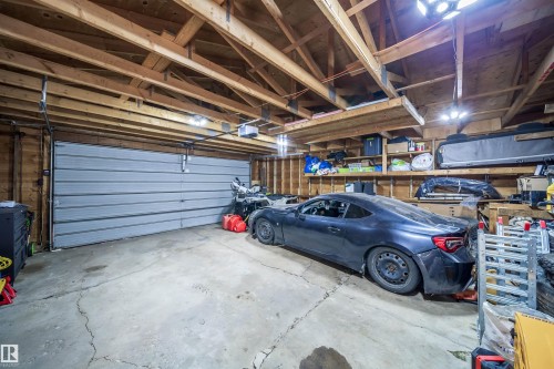 Attached two-car garage featuring a sectional garage door, exposed wood beam ceiling, concrete flooring, built-in shelving, and overhead lighting - 6403 132 Street, Edmonton, AB - Indoor Photo Showing Garage