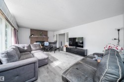 Spacious living area featuring a brick fireplace, large picture windows, wood-finish flooring, and crisp white walls - 