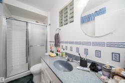 Bathroom featuring a walk-in shower with sliding glass doors, a vanity with an integrated sink, a large circular wall mirror, and a decorative tile backsplash - 