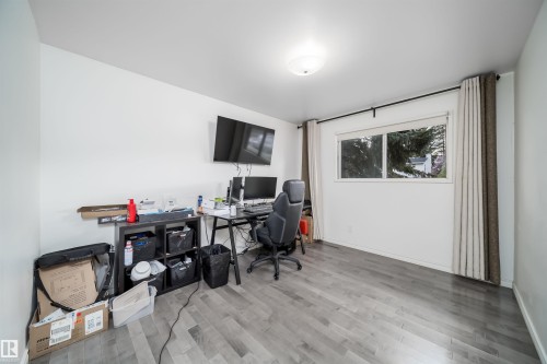 Spacious room featuring light gray wood-finish flooring, white painted walls, a flush-mount ceiling light fixture, and a large window with privacy drapes - 6403 132 Street, Edmonton, AB - Indoor Photo Showing Office