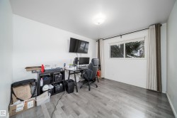 Spacious room featuring light gray wood-finish flooring, white painted walls, a flush-mount ceiling light fixture, and a large window with privacy drapes - 
