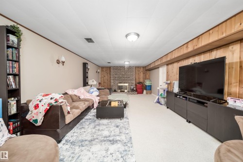 Spacious recreation room featuring a brick fireplace surround, wood paneling, and wall-mounted sconces - 6403 132 Street, Edmonton, AB - Indoor