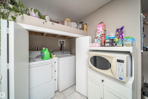 Laundry closet with bi-fold doors, white ceramic tile flooring, and overhead storage - 6403 132 Street, Edmonton, AB - Indoor Photo Showing Laundry Room