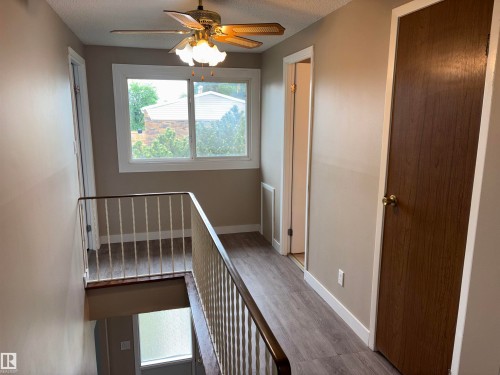 Upper-level landing featuring wood-finish flooring, a ceiling fan with integrated lighting, a large window, white trim, and a warm neutral wall color - 167 Ridgewood, St. Albert, AB - Indoor Photo Showing Other Room