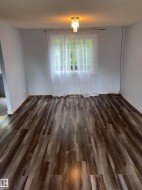 Spacious interior room featuring wood-finish flooring, light blue wall paint, and crisp white baseboards - 