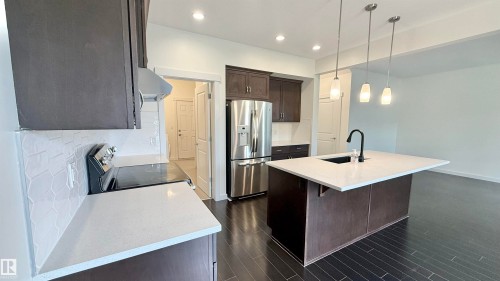Modern kitchen featuring dark wood-finish cabinetry, stainless steel appliances, and light-toned countertops - 3962 Claxton Loop, Edmonton, AB - Indoor Photo Showing Kitchen With Stainless Steel Kitchen