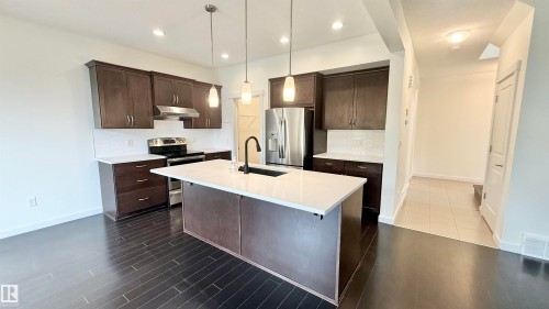 Open-concept kitchen featuring dark wood-finish cabinetry, white countertops, and a central island with a black faucet - 3962 Claxton Loop, Edmonton, AB - Indoor Photo Showing Kitchen With Stainless Steel Kitchen With Upgraded Kitchen