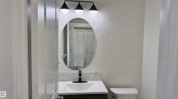 Bathroom featuring a modern vanity with a white countertop, oval mirror, and a three-light fixture - 