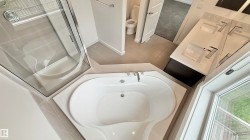 Spacious bathroom featuring a corner soaking tub, glass-enclosed shower, dual vanity with undermount sinks, and a window providing natural light - 