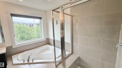 Built-in soaking tub with deck-mounted faucet, glass-enclosed shower, large window with roller shade, and light-toned wall tiling - 