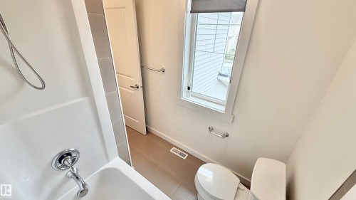 Bathroom featuring a white bathtub, chrome fixtures, a window with a roller shade, a toilet, and light-toned floor tiling - 3962 Claxton Loop, Edmonton, AB - Indoor Photo Showing Bathroom