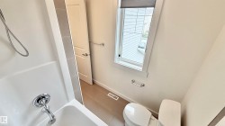 Bathroom featuring a white bathtub, chrome fixtures, a window with a roller shade, a toilet, and light-toned floor tiling - 
