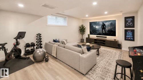 Brightly lit recreation room featuring recessed lighting, a large window with blinds, light wood-finish flooring, and a media console - 3962 Claxton Loop, Edmonton, AB - Indoor Photo Showing Gym Room