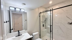 Modern bathroom featuring a glass-enclosed shower with matte black hardware and white marble-look tile - 