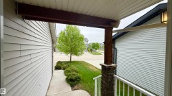 Covered front porch featuring a stone-clad post, wood beam accents, and white railings - 