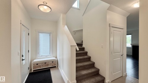 Foyer entry featuring ceramic tile flooring, a window with horizontal blinds, and a carpeted staircase with white risers - 3962 Claxton Loop, Edmonton, AB - Indoor Photo Showing Other Room