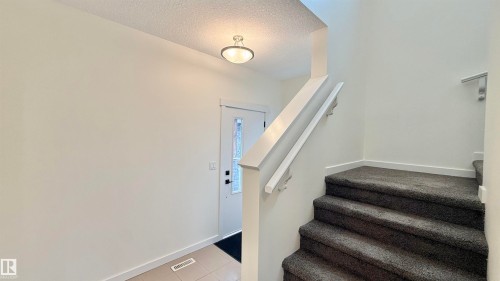 Entrance foyer with a staircase featuring dark gray carpeting and white handrails - 3962 Claxton Loop, Edmonton, AB - Indoor Photo Showing Other Room