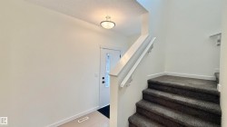 Entrance foyer with a staircase featuring dark gray carpeting and white handrails - 