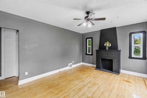 Spacious room featuring wood-finish flooring, a contemporary ceiling fan, and a prominent black fireplace with a mantel - 11842 93 Street, Edmonton, AB 