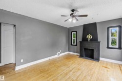 Spacious room featuring wood-finish flooring, a contemporary ceiling fan, and a prominent black fireplace with a mantel - 