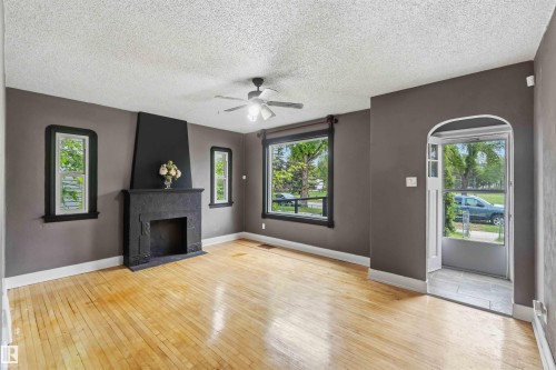 Spacious living area featuring light wood flooring, a decorative fireplace with a dark surround, and a ceiling fan - 11842 93 Street, Edmonton, AB 