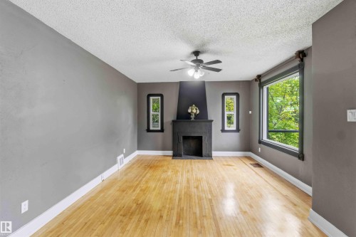 Living area featuring wood-finish flooring, a central fireplace with a dark mantel, multiple windows, a ceiling fan with integrated lighting, and crown molding accents - 11842 93 Street, Edmonton, AB 