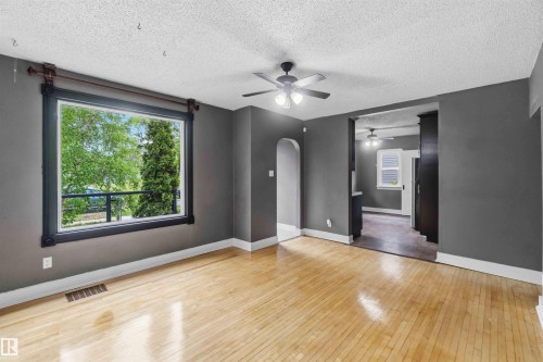 Spacious room with light wood-finish flooring, dark grey walls, and white baseboards - 11842 93 Street, Edmonton, AB 