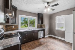 Kitchen featuring dark wood-finish cabinetry, stainless-steel appliances, a stacked stone-look backsplash, and a double basin sink - 