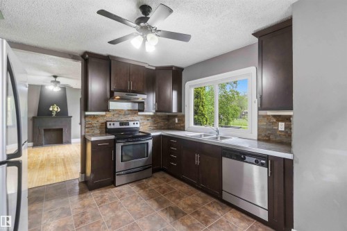 Kitchen featuring dark wood-finish cabinetry, stainless steel appliances, mosaic tile backsplash, a double basin sink, and tile flooring - 11842 93 Street, Edmonton, AB 