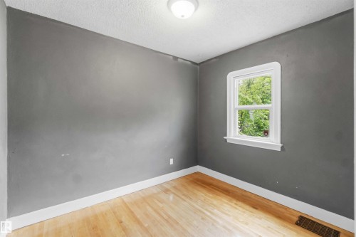 Interior space featuring wood-finish flooring, a single pane window with white trim, and a ceiling-mounted light fixture - 11842 93 Street, Edmonton, AB 