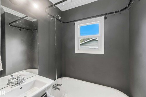 Bathroom featuring a white freestanding clawfoot tub, a single window with white trim, and a wall-mounted pedestal sink with chrome fixtures - 11842 93 Street, Edmonton, AB 