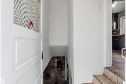White paneled door with a diamond-patterned mesh insert, opening to a descending staircase with concrete flooring - 11842 93 Street, Edmonton, AB 