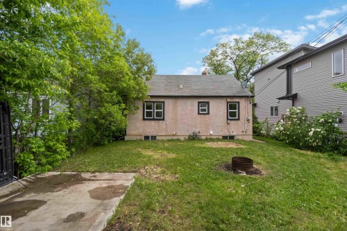 Rear exterior of a stucco home featuring a shingle roof and multiple windows with dark trim - 11842 93 Street, Edmonton, AB 