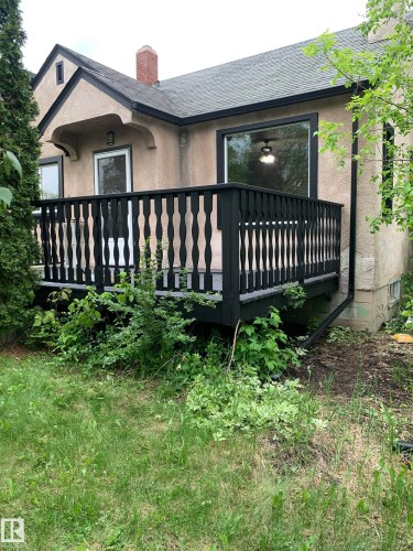 Rear exterior featuring a black-painted wooden deck with decorative balusters, stucco siding, and a large picture window with black trim - 11842 93 Street, Edmonton, AB 