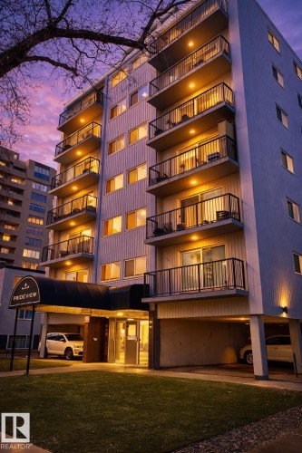 Multi-story building featuring multiple private balconies with black railings, a ground-level covered entry, and integrated covered parking - 202 8310 Jasper Avenue, Edmonton, AB - Outdoor With Balcony