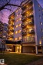Multi-story building featuring multiple private balconies with black railings, a ground-level covered entry, and integrated covered parking - 202 8310 Jasper Avenue, Edmonton, AB  - Outdoor With Balcony 