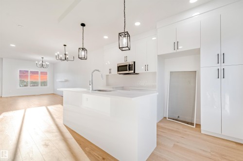 Modern kitchen featuring a central island, stainless steel microwave, white high-gloss cabinetry, and wood-finish flooring - 1511 211 Street Nw, Edmonton, AB 