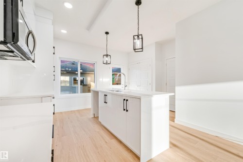 Kitchen featuring a center island, pendant lighting, built-in microwave, wood-finish flooring, and white cabinetry - 1511 211 Street Nw, Edmonton, AB 