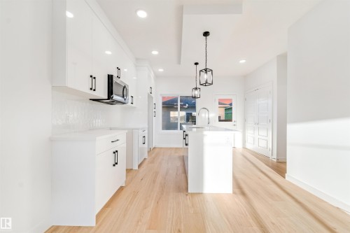 Contemporary kitchen featuring recessed lighting, a smooth white tile backsplash, an integrated microwave, a center island with a sink, and wood-finish flooring - 1511 211 Street Nw, Edmonton, AB 