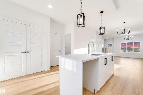 Kitchen island with a stainless steel sink and gooseneck faucet, light wood-finish flooring, recessed lighting, and modern pendant light fixtures - 1511 211 Street Nw, Edmonton, AB 