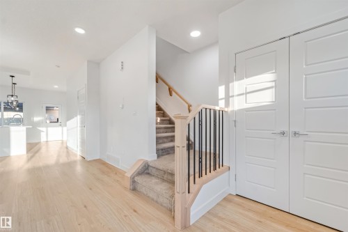 Light wood-finish flooring throughout, carpeted staircase with wood handrail and black metal balusters, recessed lighting, and white paneled doors - 1511 211 Street Nw, Edmonton, AB 