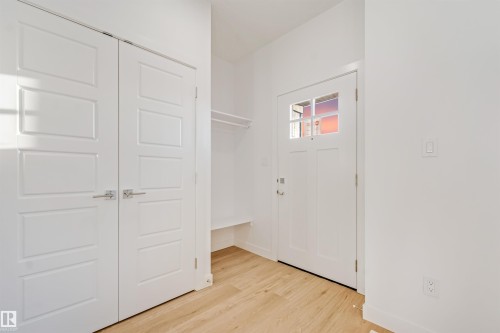 Entryway featuring wood-finish flooring, a solid white door with glass panels, and a built-in storage bench with an overhead clothing rod - 1511 211 Street Nw, Edmonton, AB 