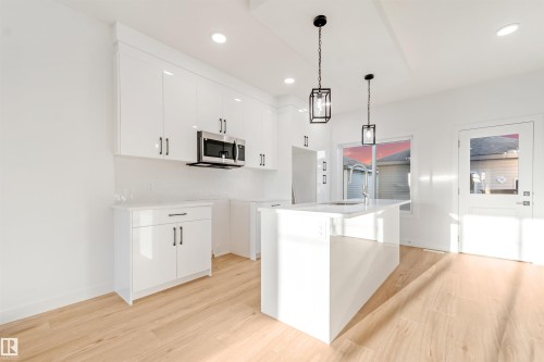 Bright kitchen featuring white cabinetry, a large center island with an undermount sink, stainless steel built-in microwave, wood-finish flooring, and recessed lighting - 1511 211 Street Nw, Edmonton, AB 