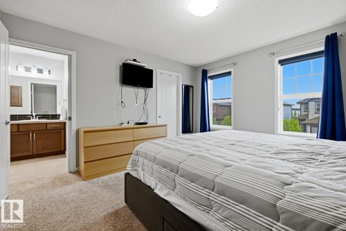 Bedroom featuring two windows, carpeted flooring, and a door opening to a bathroom with a wood-finish vanity and tile flooring - 17844 61 Street, Edmonton, AB 
